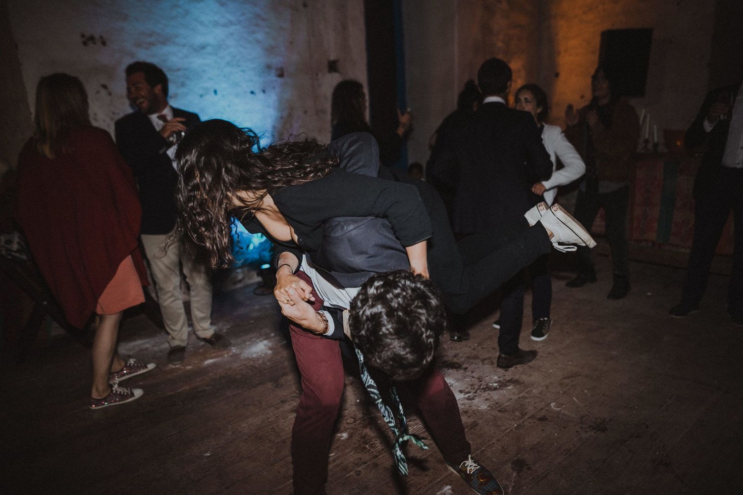 People dancing and moving energetically in a dimly lit indoor venue during a celebration.