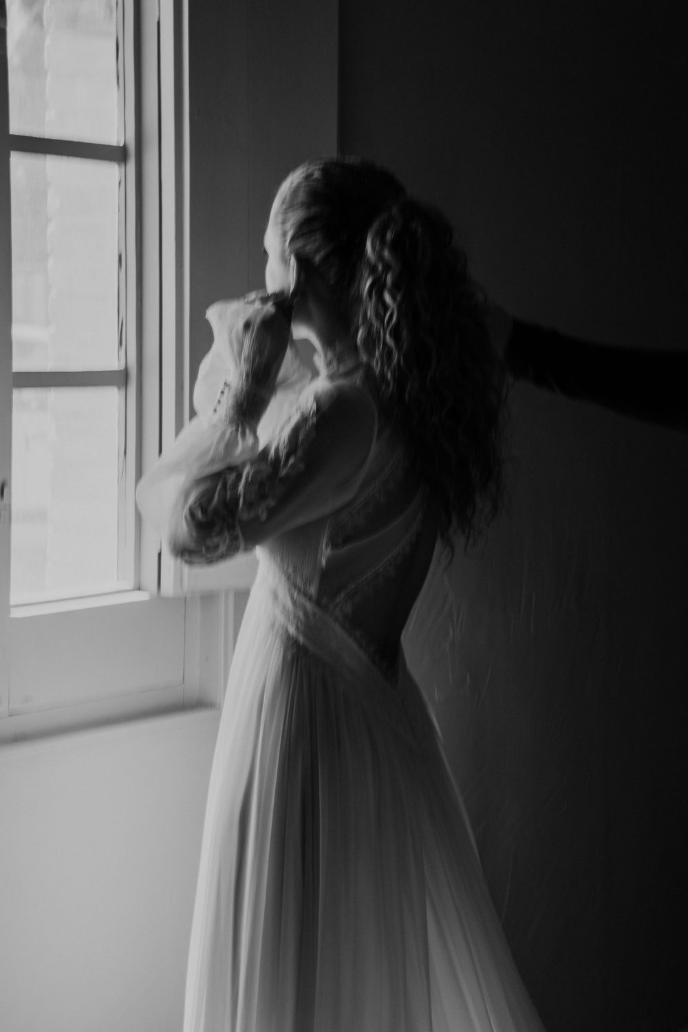 Artistic black and white photo of flowing white dress movement near a window.