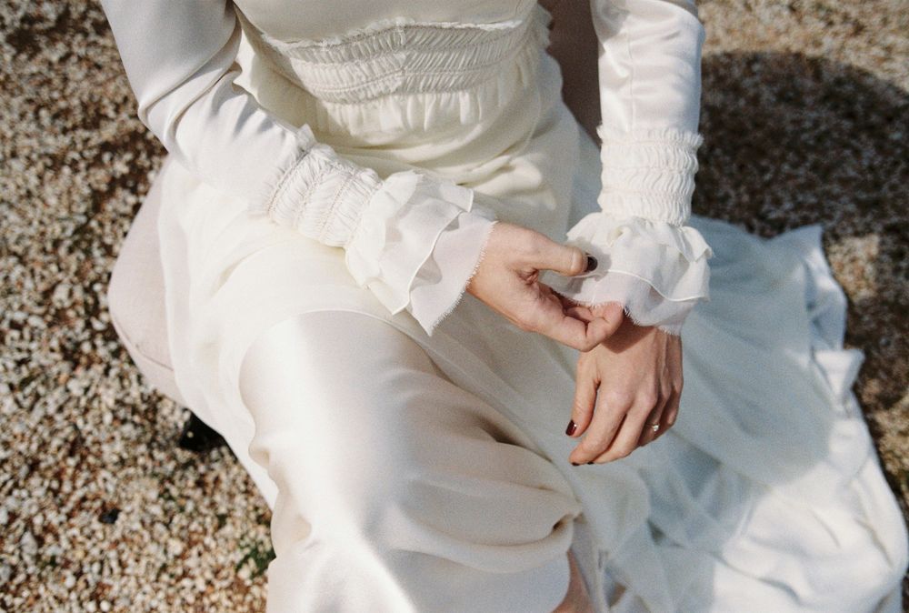 Close-up detail of hands resting on a white wedding dress fabric.