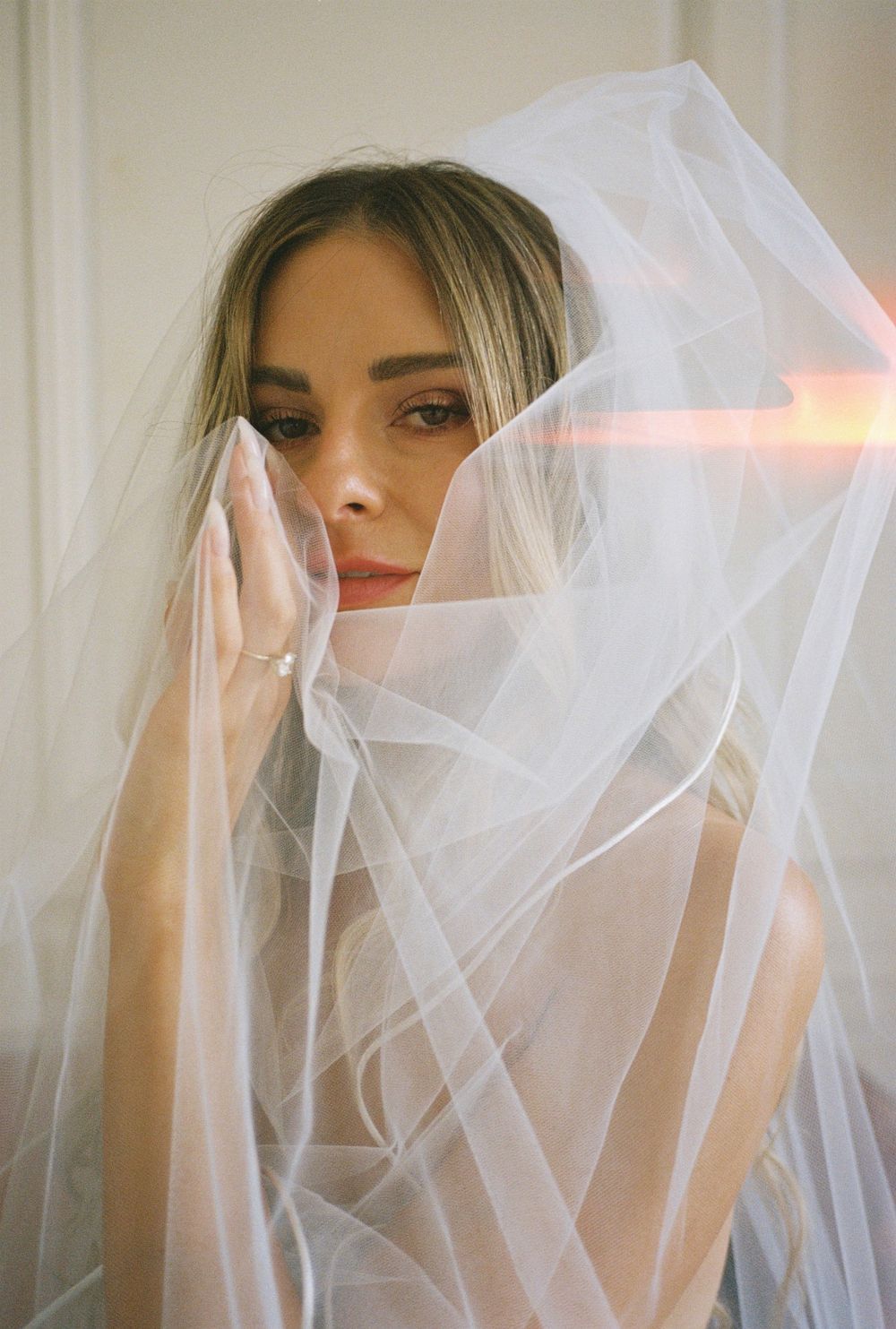 Ethereal bridal portrait through delicate white tulle veil.
