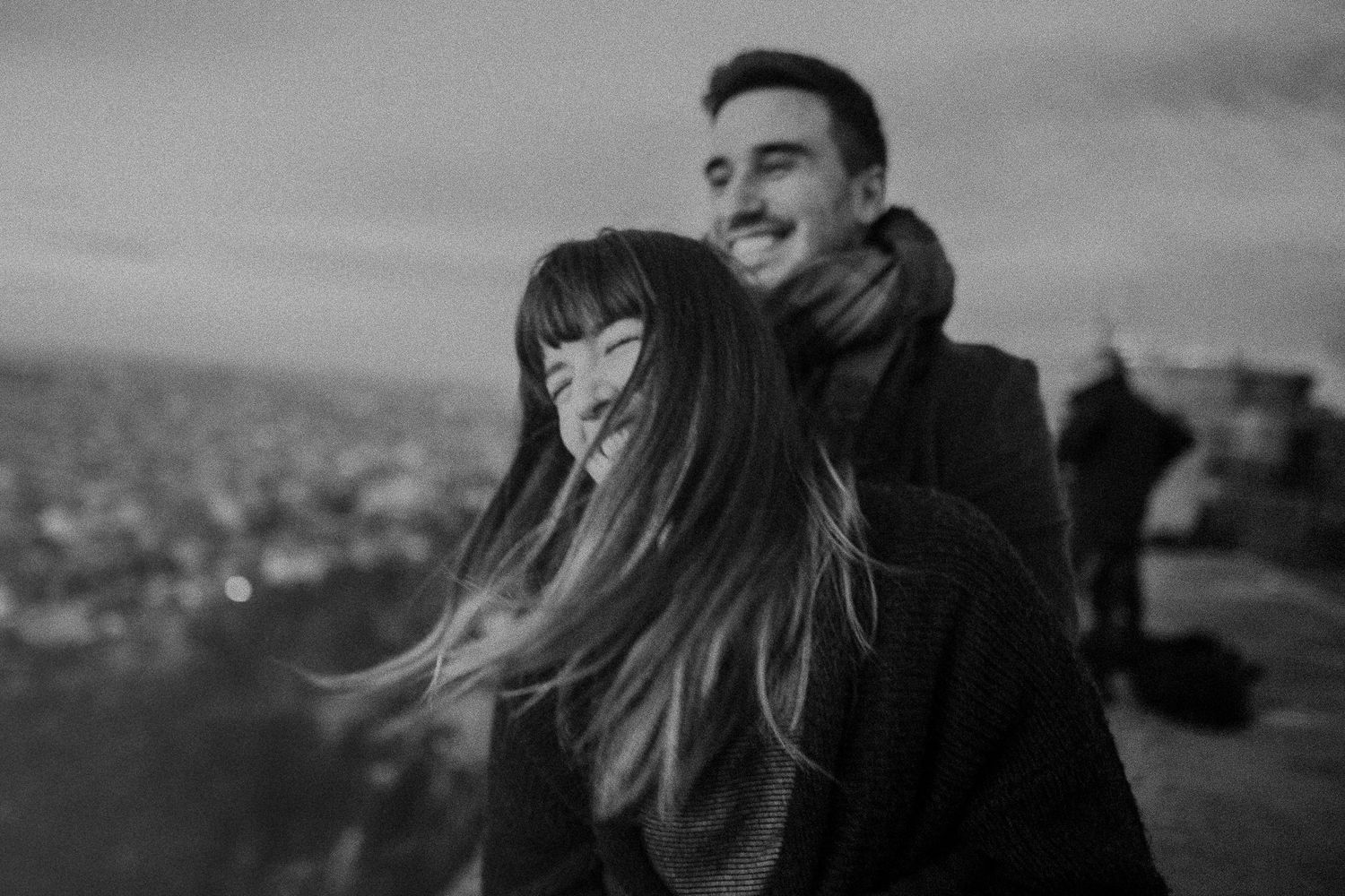 A couple shares a tender moment against a city backdrop at dusk.