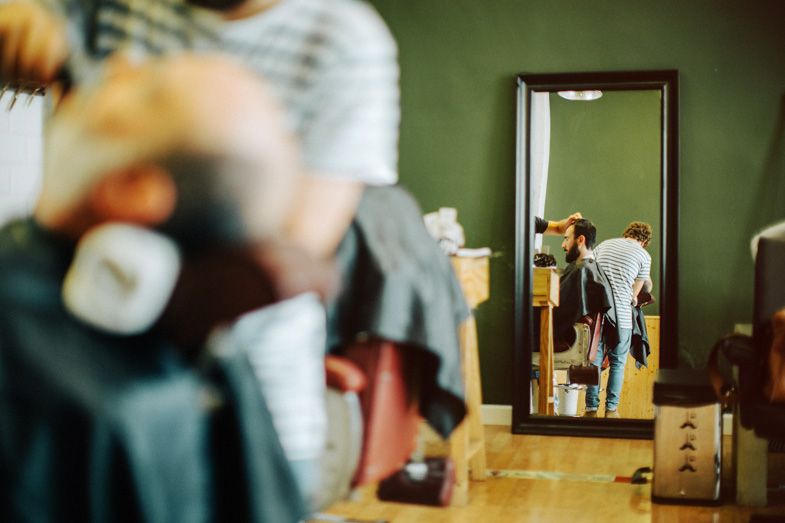 Mirror reflection in a barbershop showing people working in the background.