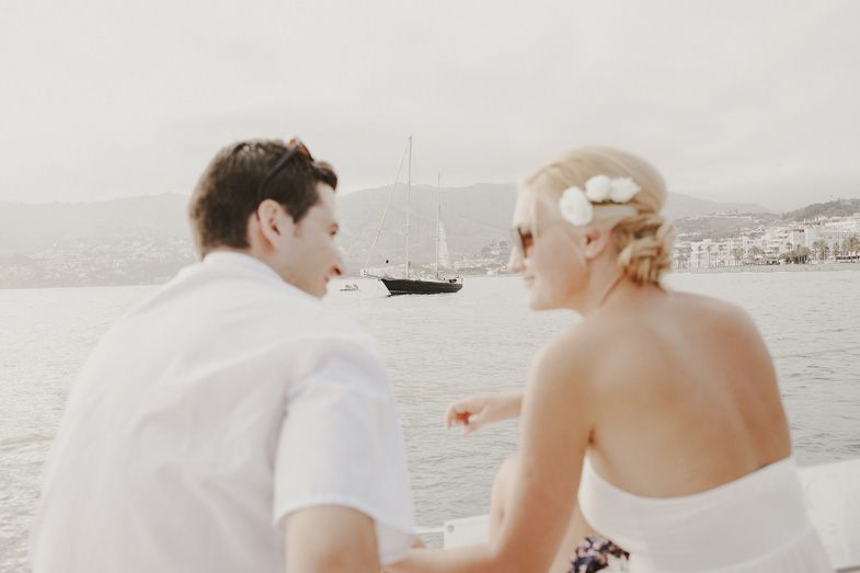 A couple sitting together overlooking a scenic harbor with a boat in the distance.