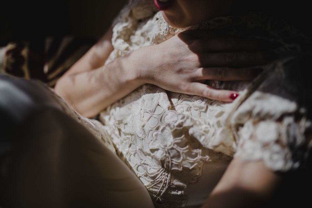 Intimate close-up of lace wedding dress details and hands.