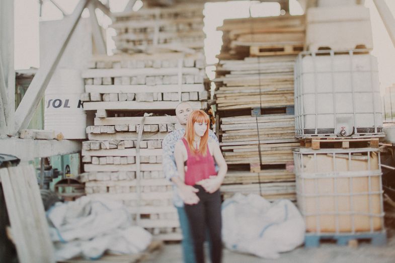 A person stands among stacked wooden pallets and industrial storage materials.