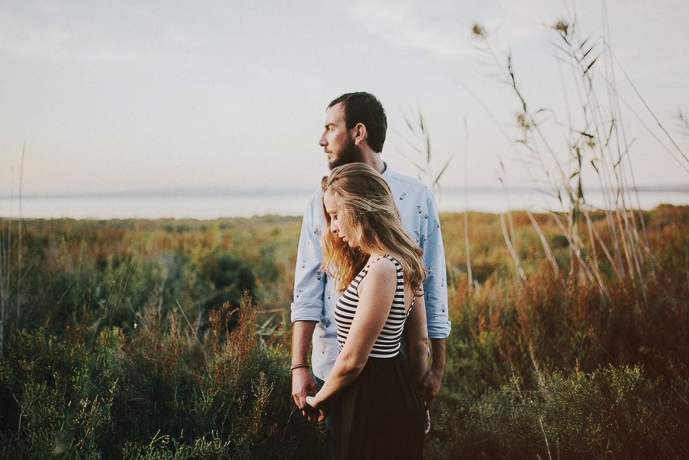 Couple embracing in a field of tall grass during golden hour.