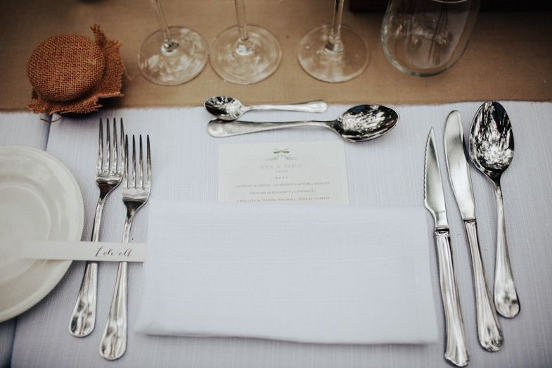 Elegant place setting with formal silverware, plates, and glasses on white tablecloth.