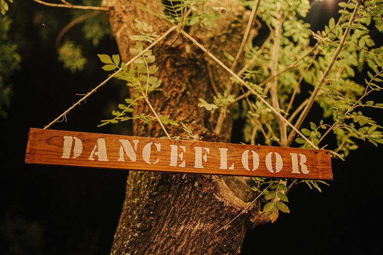 Wooden sign reading 'DANCEFLOOR' hanging from a tree branch at an outdoor event.