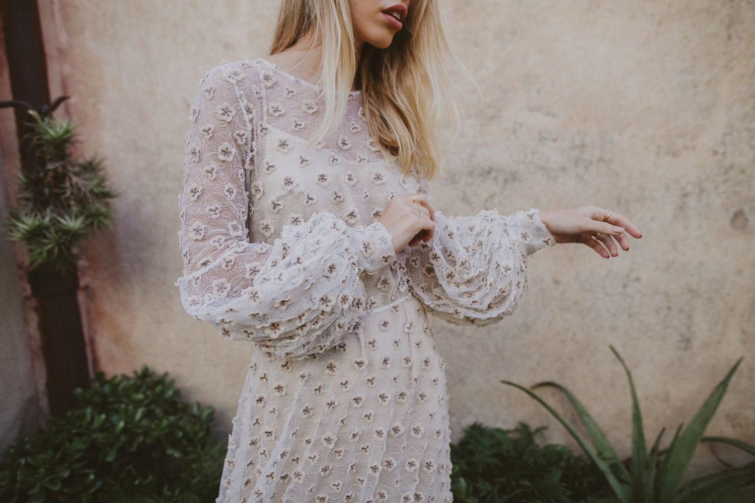 A vintage-inspired white lace dress with long bell sleeves and intricate floral details.