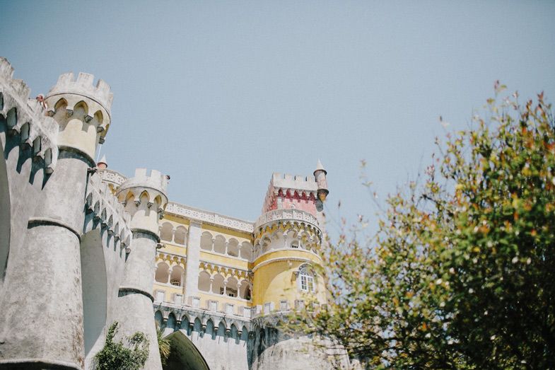 White stone towers and yellow walls of Pena Palace with blooming spring flowers in foreground.