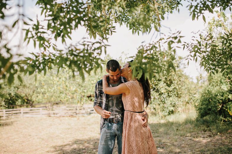 A couple sharing an intimate moment on a sunlit path surrounded by trees.