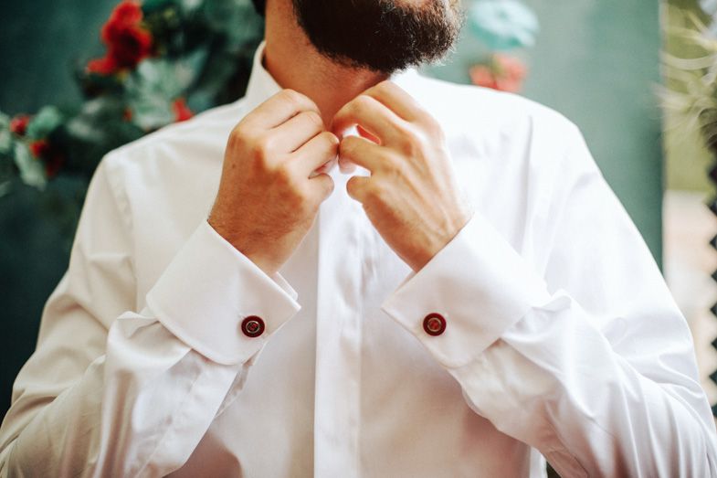 Close-up of white dress shirt with burgundy buttons being fastened.