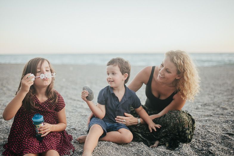 Family blowing bubbles together on beach during sunset.