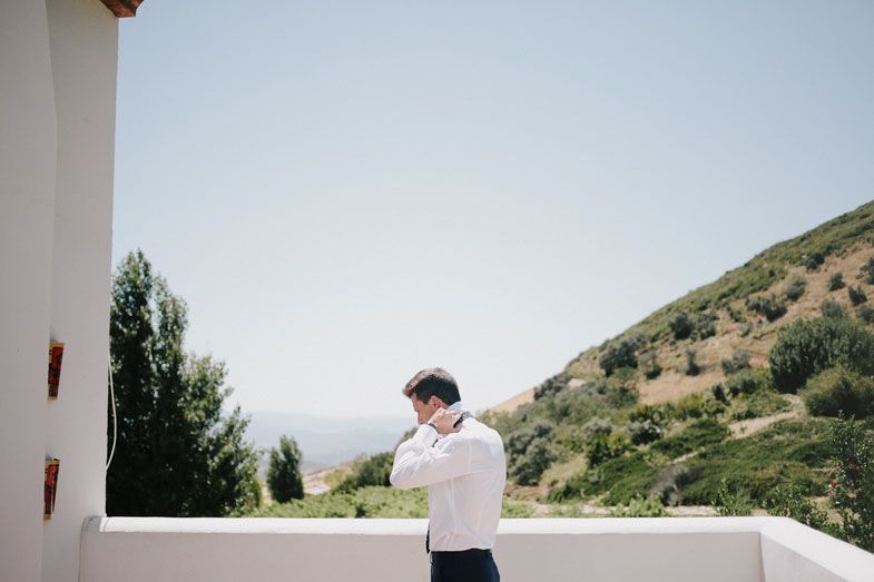 Person in formal attire adjusts clothing on balcony with mountain view.