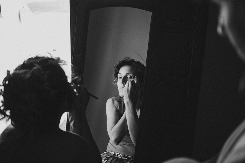 Black and white photo of someone getting their makeup done in front of a mirror.