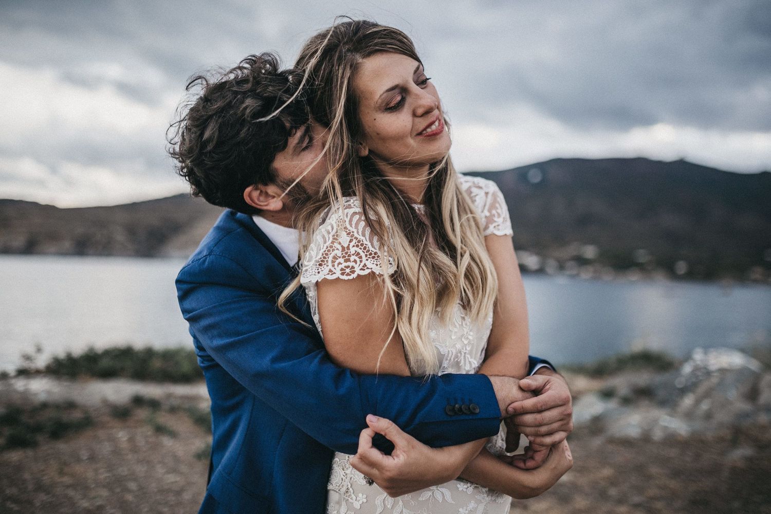 Intimate moment between newlyweds against dramatic coastal landscape and cloudy sky.