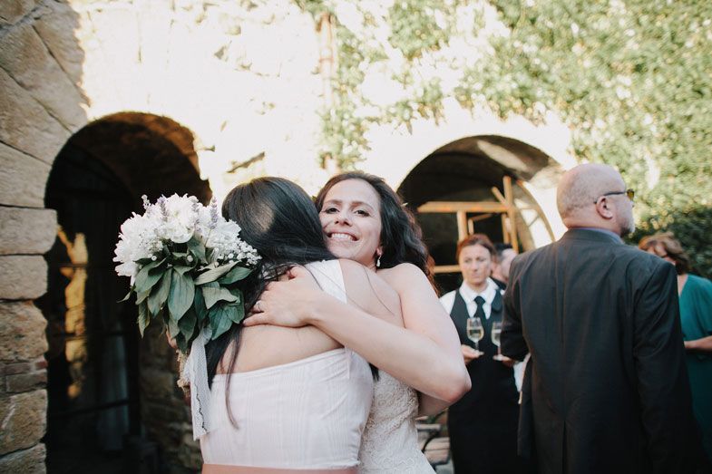 Two people share an emotional embrace at an outdoor wedding ceremony with stone archways and greenery in the background.