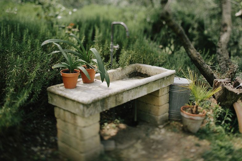 Rustic stone garden bench with potted plants in a lush green setting.