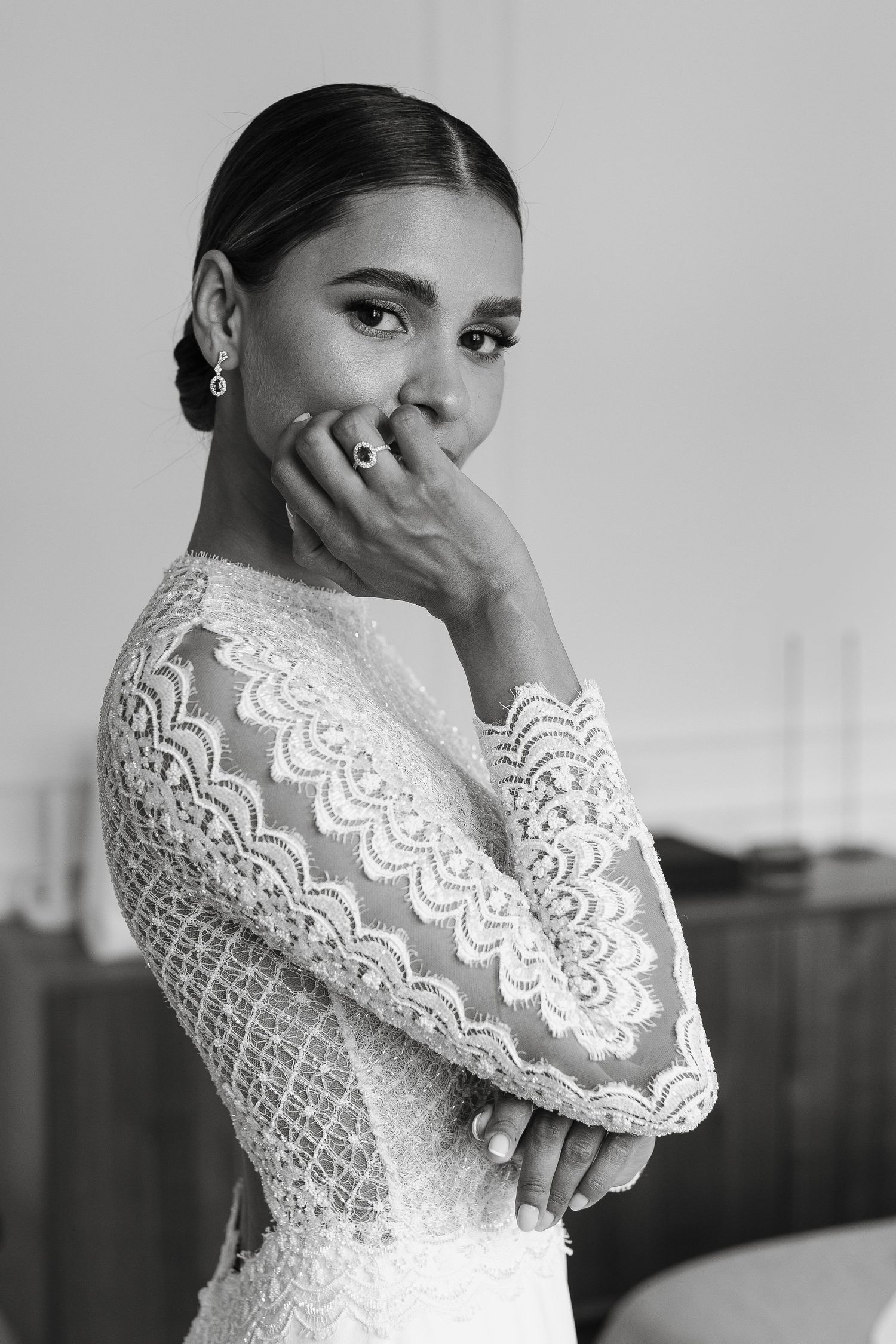 Black and white portrait of someone in an elegant lace wedding dress with intricate long sleeves and delicate details.