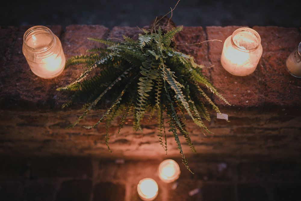 Fern centerpiece decoration with glowing candles on rustic wooden surface creating moody ambiance.