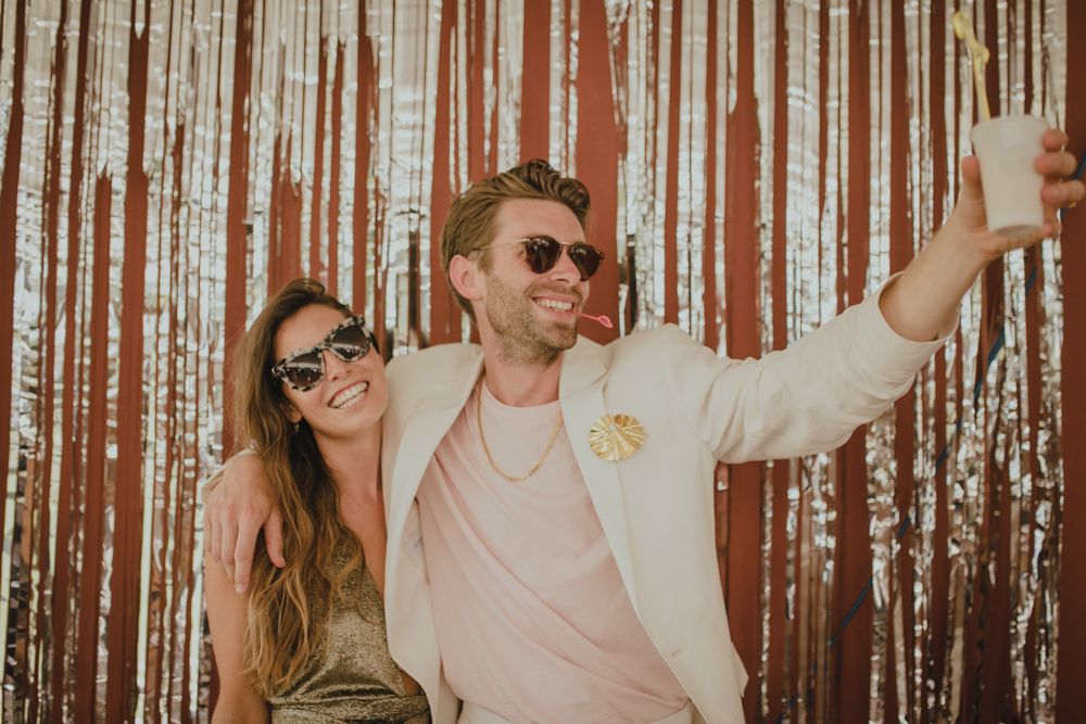 Couple in sunglasses posing playfully against a shimmering backdrop.