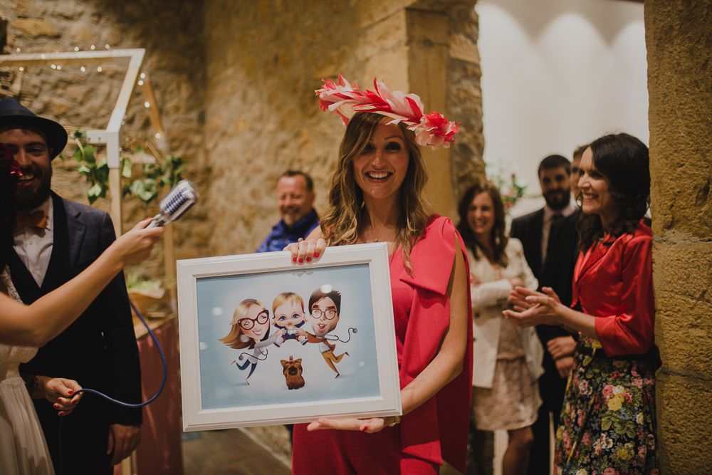 Guest in bright red dress presents framed artwork at wedding celebration.