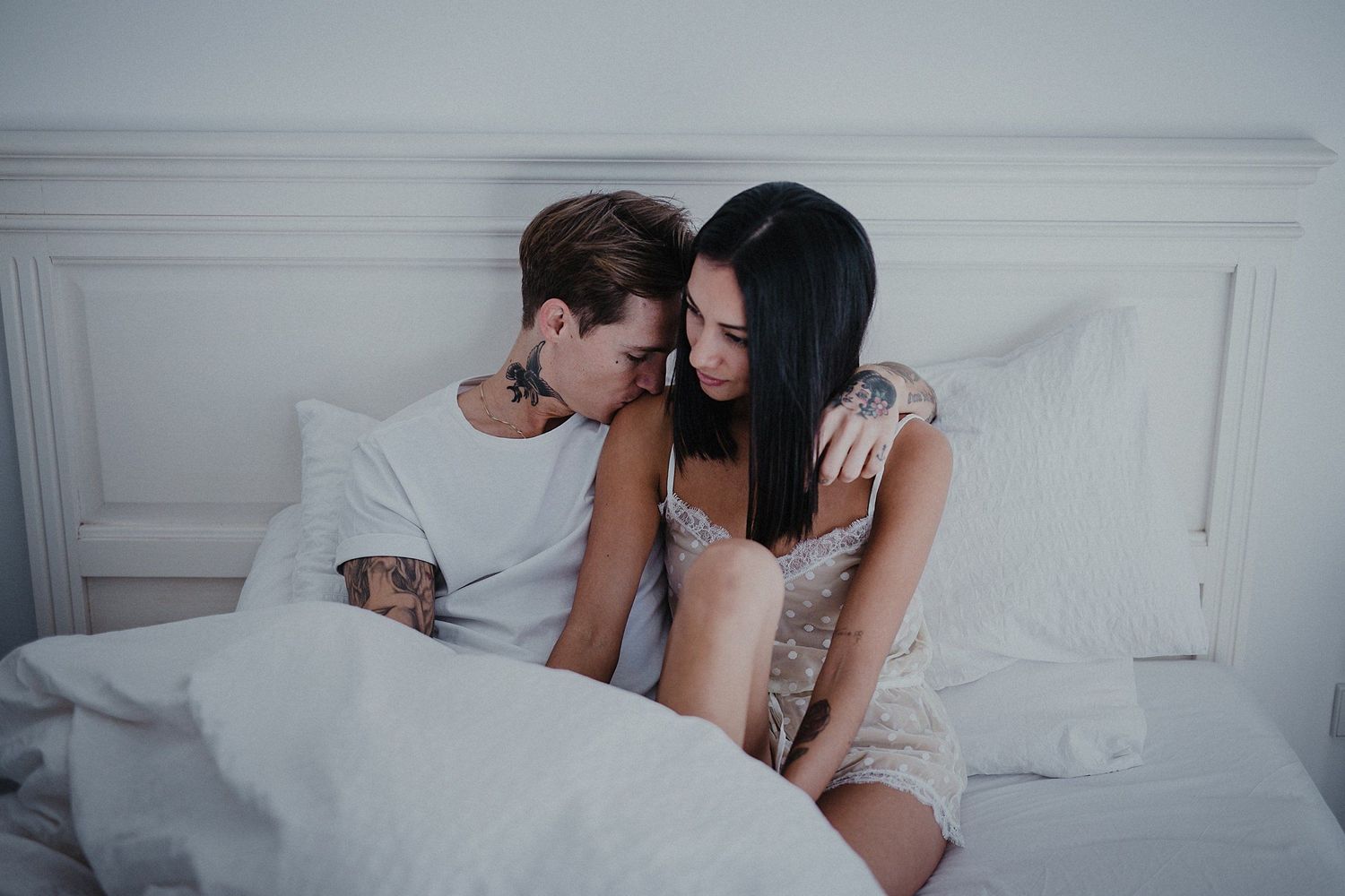 Couple in casual attire sharing tender moment on bed.