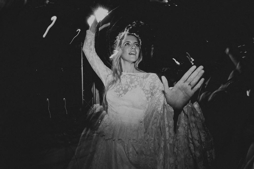 Black and white photo of bride dancing with raised arms in a lace dress.