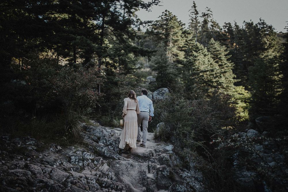 A couple walks along a rocky forest path in moody natural lighting.