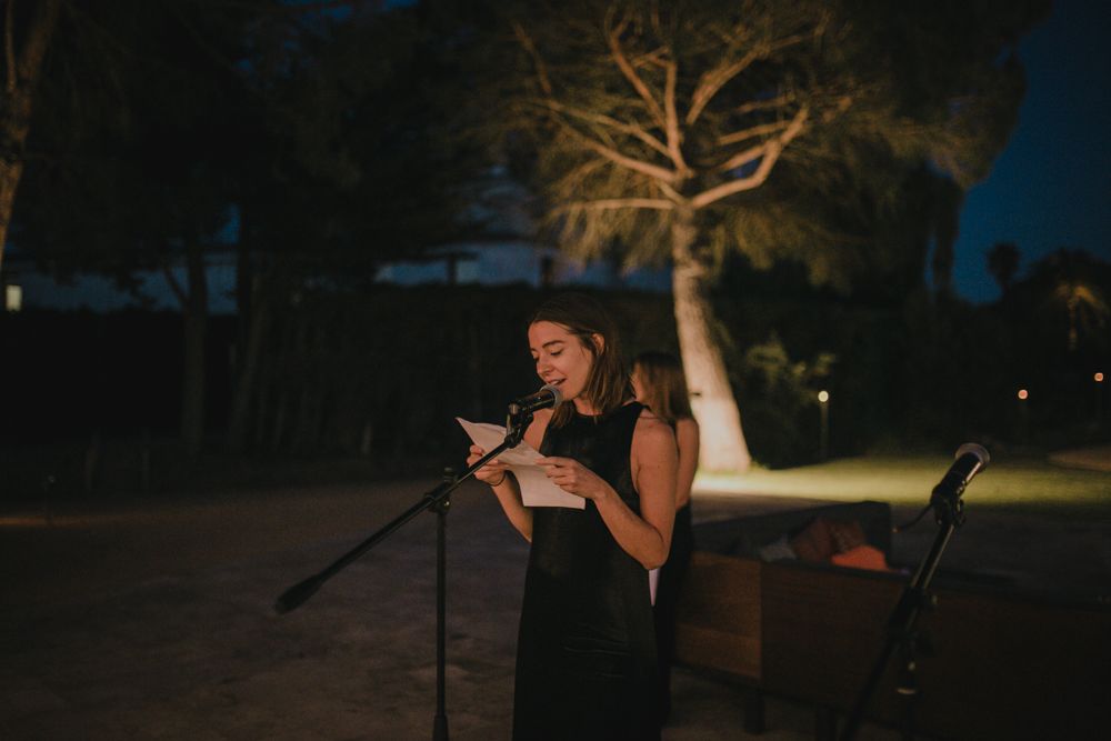 Speaker giving a speech outdoors at night with illuminated tree in background.