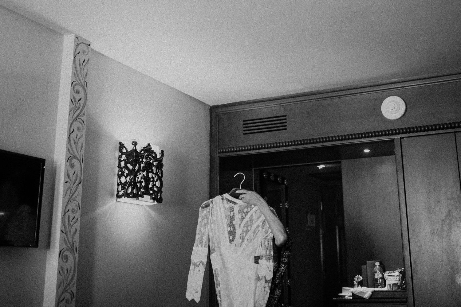 Wedding dress hanging on wall next to decorative light fixture in hotel room.