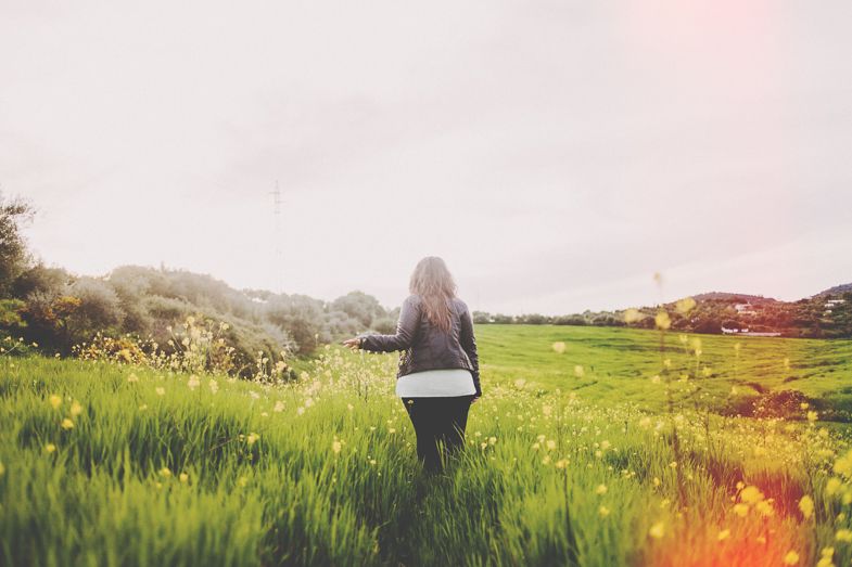 Silhouette of a person walking through a lush green meadow at sunset.