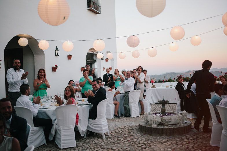 Outdoor wedding reception setup with paper lanterns and white-covered tables at sunset.