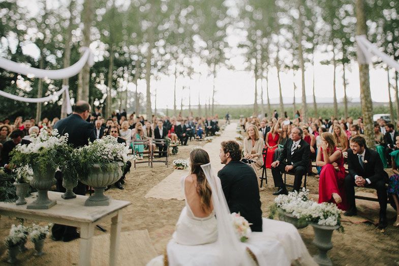 Wedding couple faces their guests during outdoor forest ceremony with decorative details.