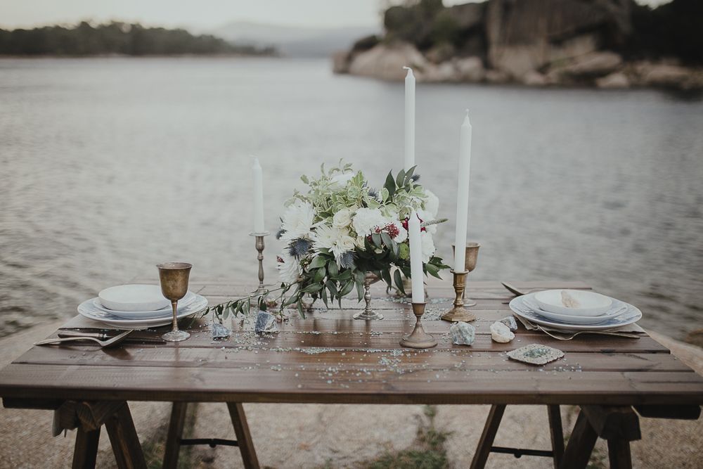 Elegant table setting with white floral centerpiece and candles overlooking a lake.