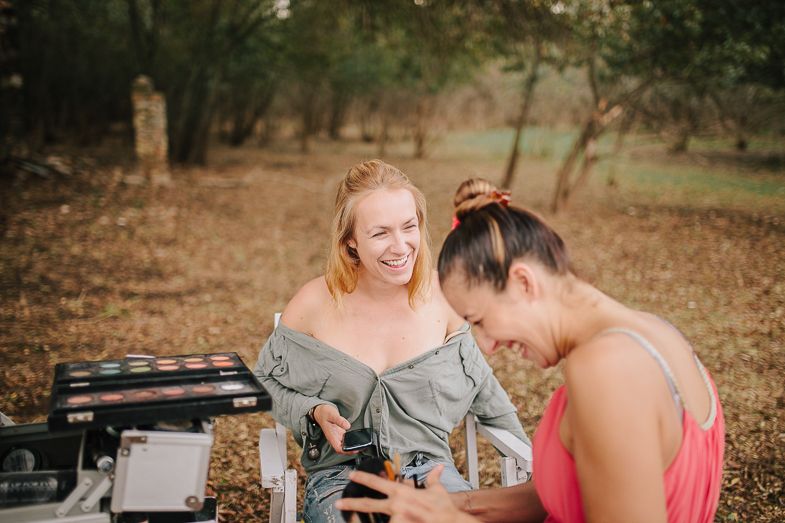 Two people working together with makeup supplies in a natural outdoor setting.
