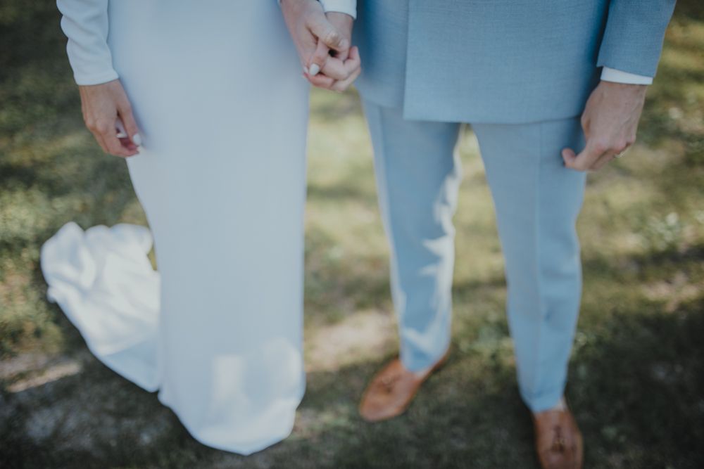 Close-up of wedding attire showing light blue suit pants and flowing white dress hem.