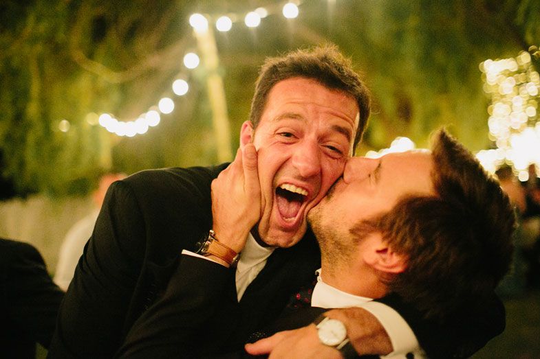 Two party guests share a joyful candid moment under string lights at night.