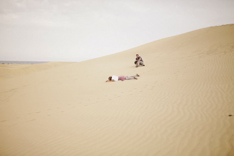 Distant figure sitting alone among vast rolling sand dunes.