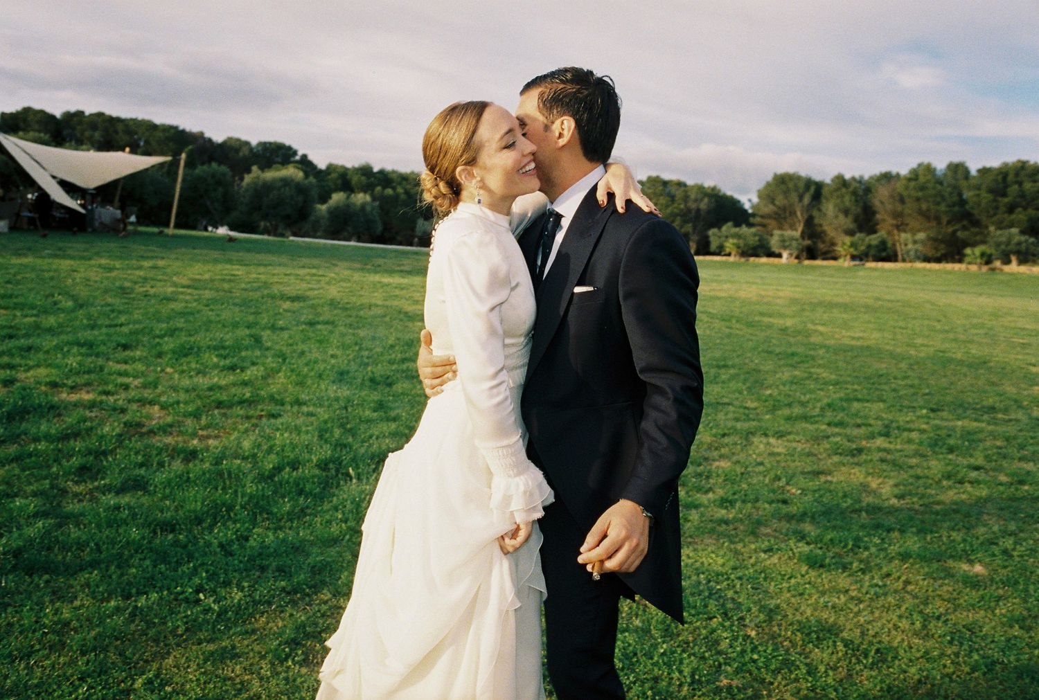 A couple in wedding attire shares a romantic moment in a lush green field on their special day.