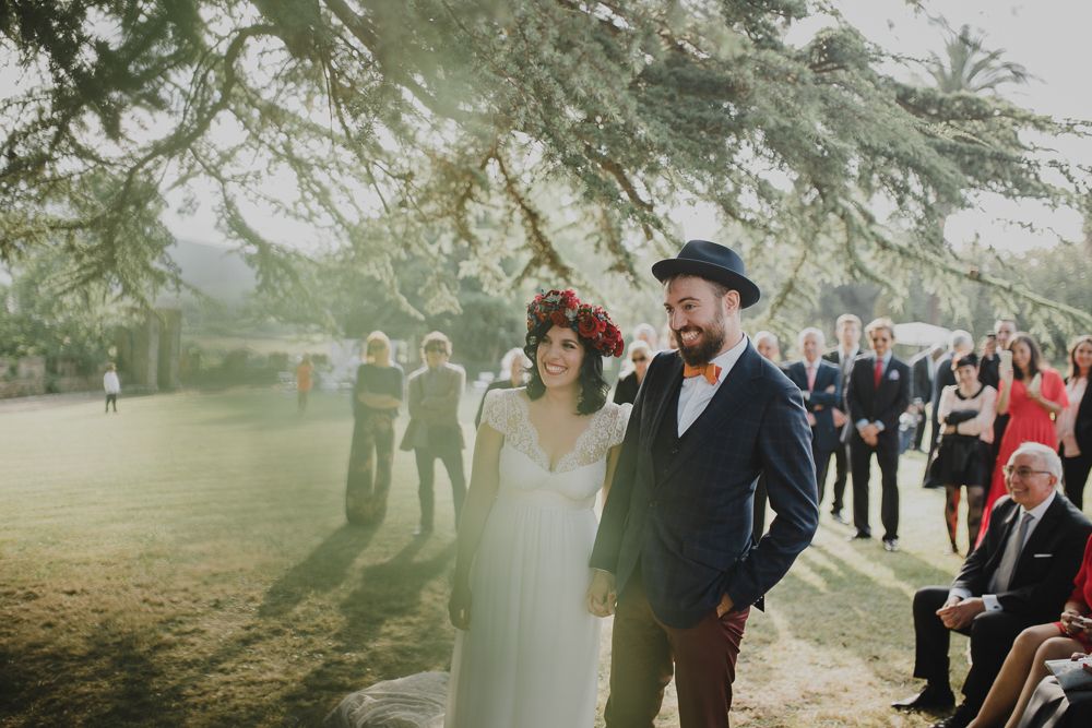 A couple walks through a misty outdoor venue with wedding guests visible in the background.