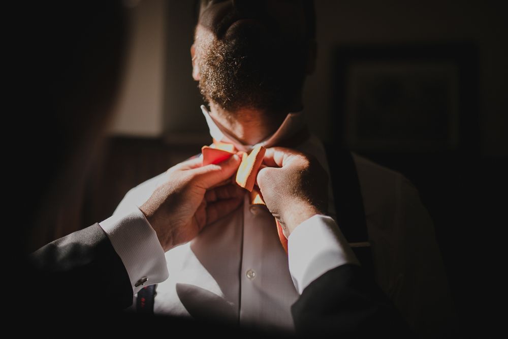 Close-up shot of someone adjusting an orange bowtie in dramatic lighting.