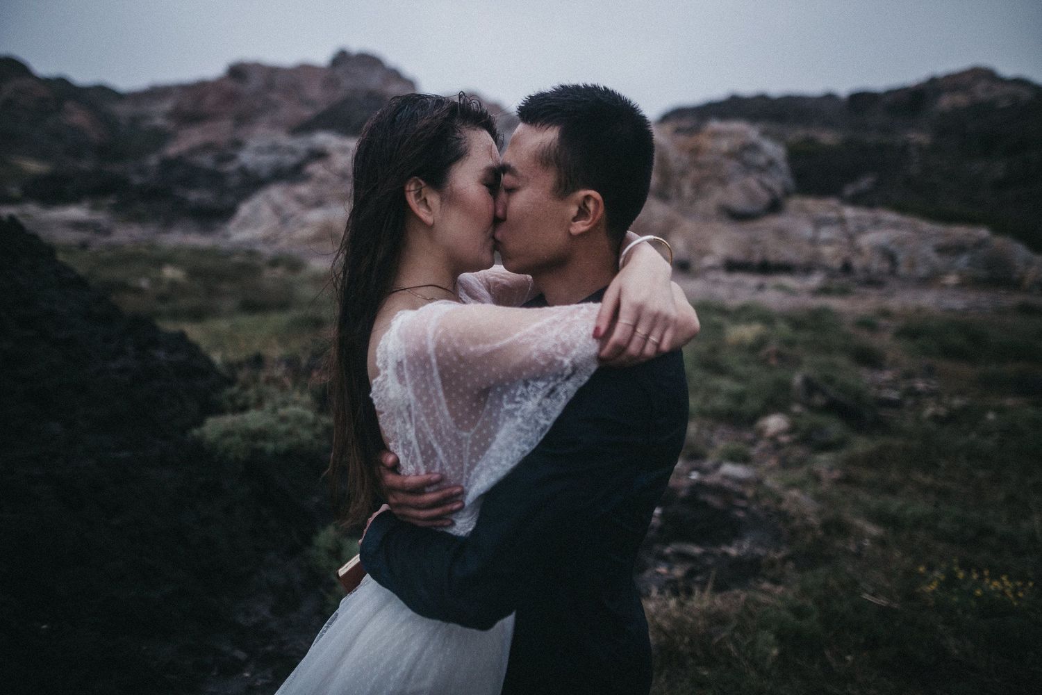 A romantic mountain-side kiss between a couple in formal attire.
