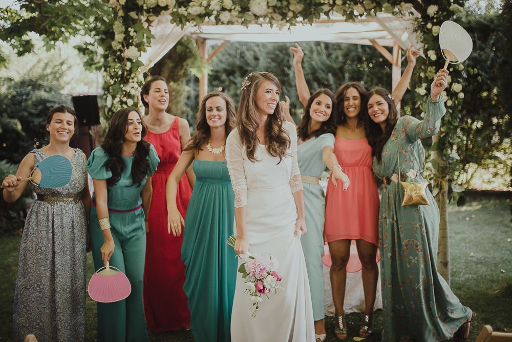 Wedding party in colorful dresses poses together at an outdoor garden celebration.