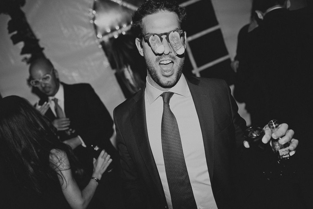 Wedding guest in glasses and suit dancing energetically at reception party.