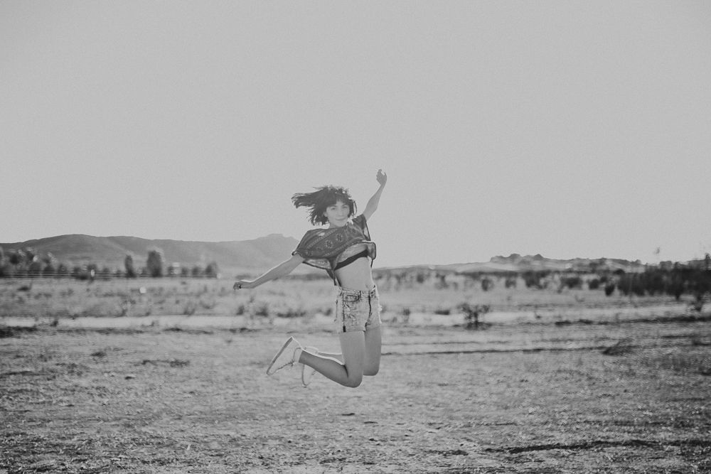 A black and white photo of someone jumping with joy in an open desert landscape.