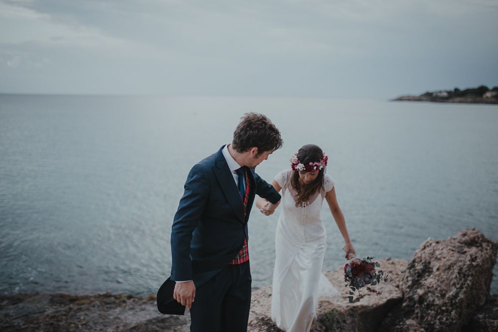 A romantic wedding couple stands on coastal rocks overlooking a misty ocean view.