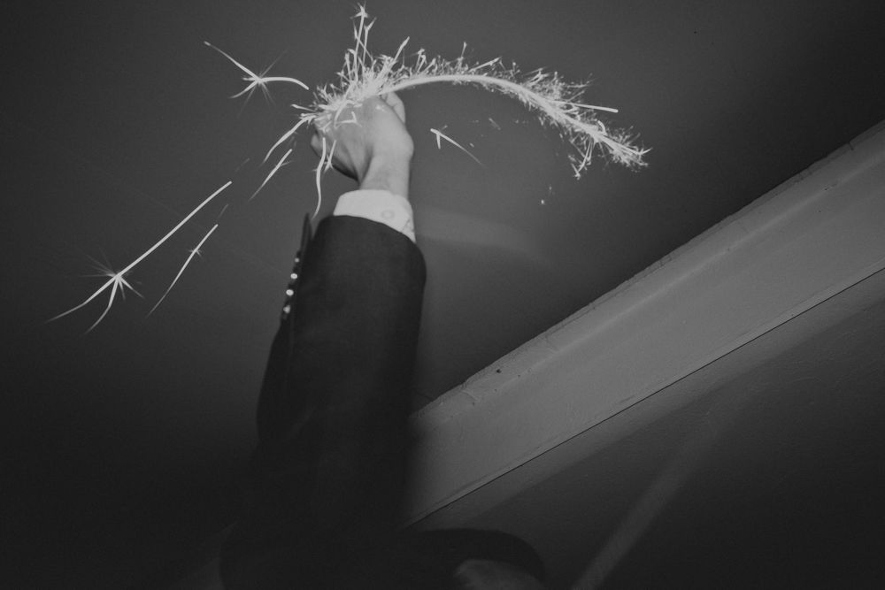 Hand holding a lit sparkler against dark ceiling, creating bright streaks of light.