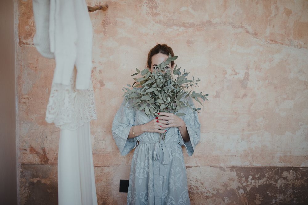 Person in blue dress holding a large bouquet of dried eucalyptus against textured pink wall.