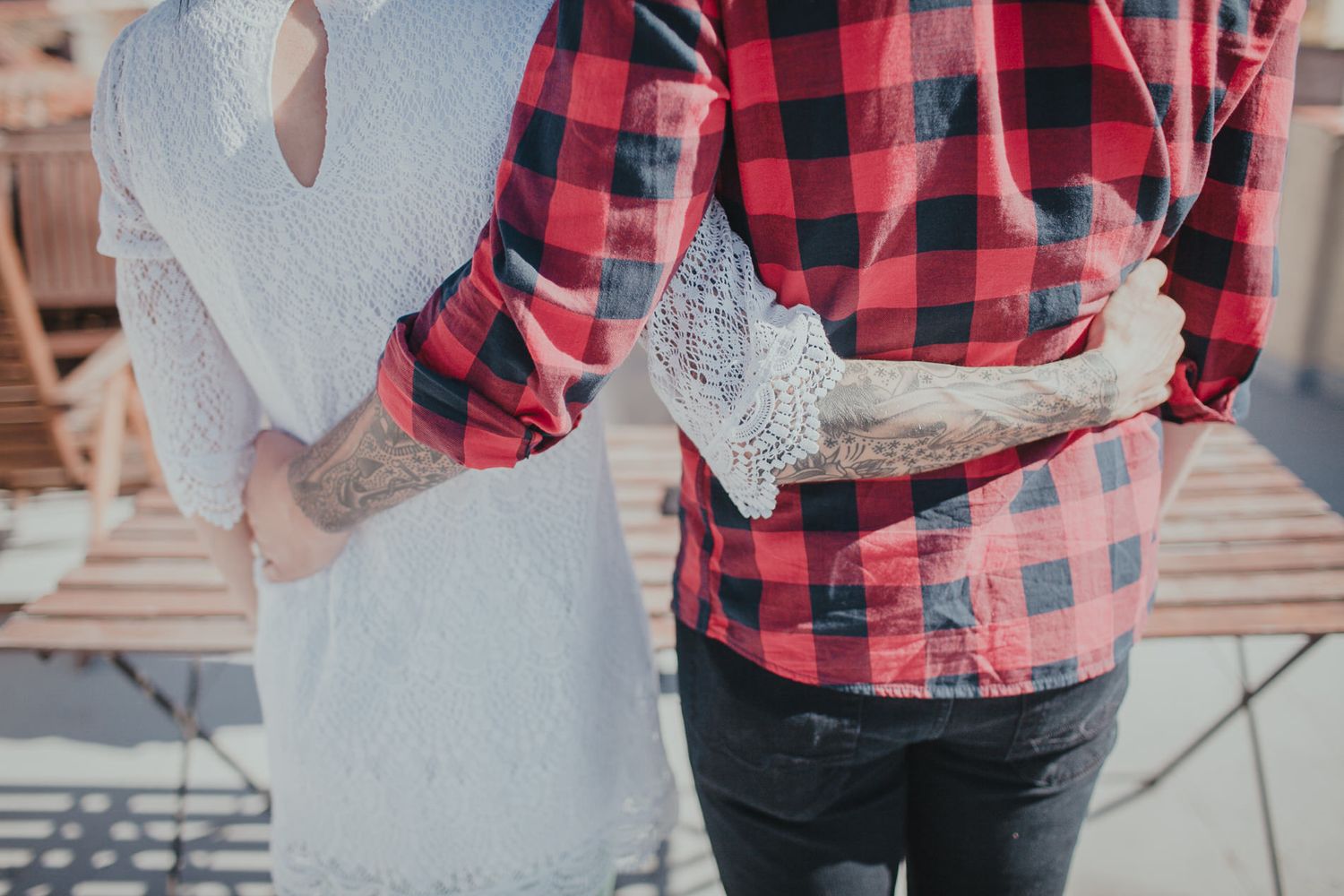 Close-up detail of hands and clothing during a rooftop embrace, featuring red plaid and white lace.